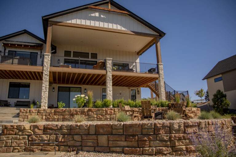 Retaining wall with plants and chairs against house.