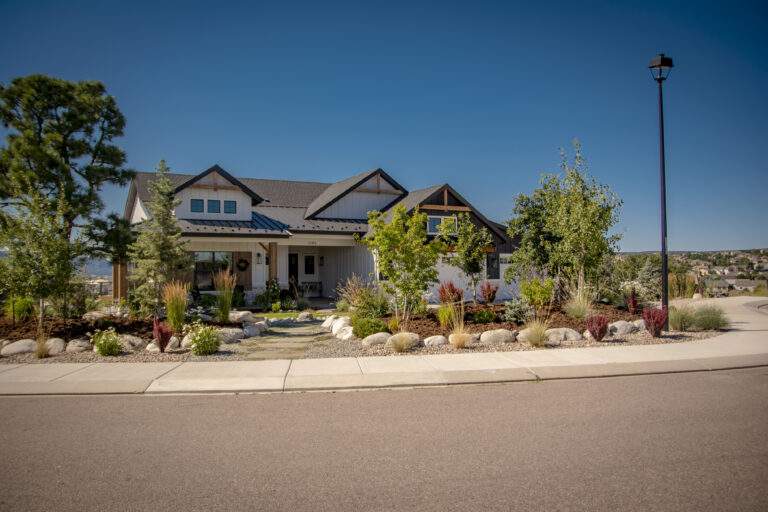 Front of home with plants, rock and trees.