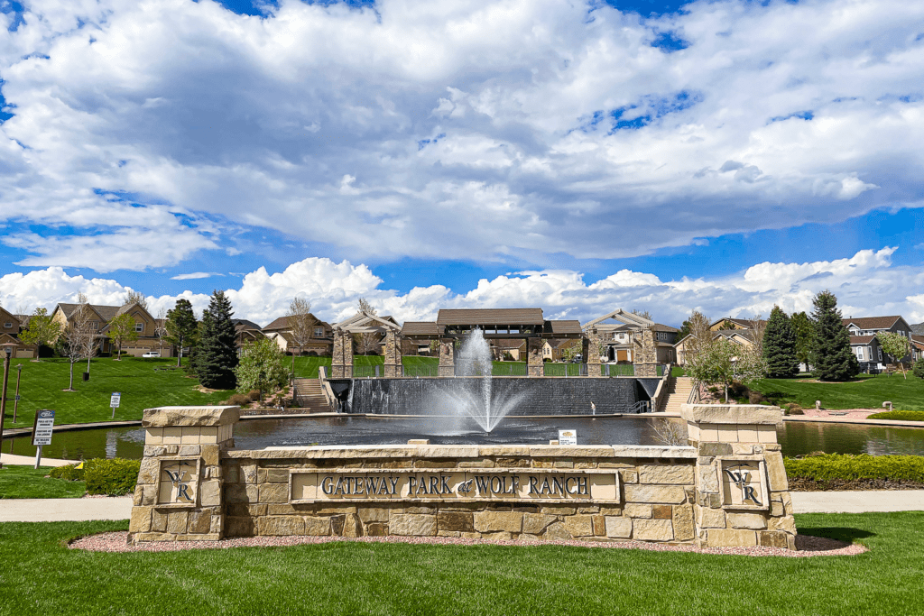 Sign for Wolf ranch with green lawn and water feature behind it